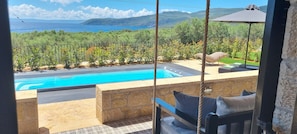 Ein Pool mit Meerblick, eine Steinsäule und ein Schaukelstuhl.