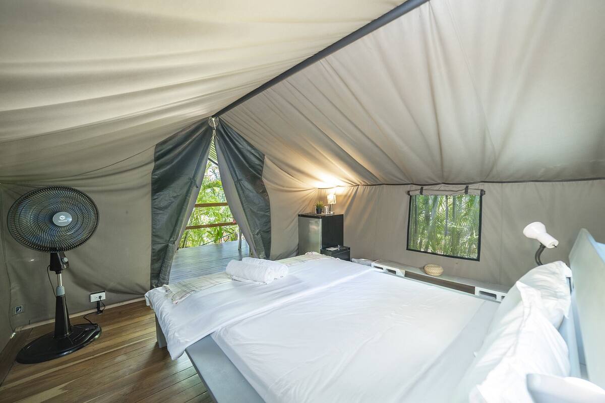 A tent with a bed, a fan, a lamp, and a window.