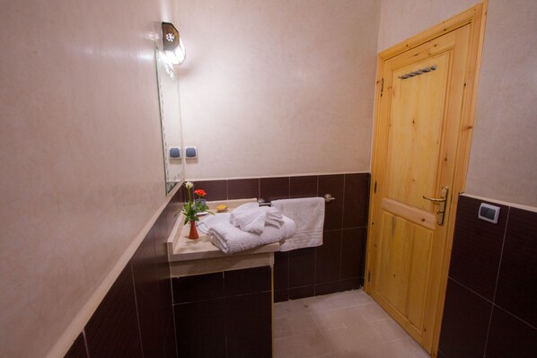 A bathroom with a wooden door, a sink with a mirror, and a towel rack.