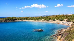 A coastal beach with clear blue waters, rocky outcrops, and a sandy shore with umbrellas.