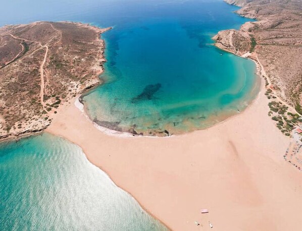 Vista aérea de una zona costera con una extensa playa de arena, aguas turquesas cristalinas y terreno rocoso.