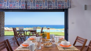 A dining table set with breakfast items, a view of the ocean, and a stone wall.