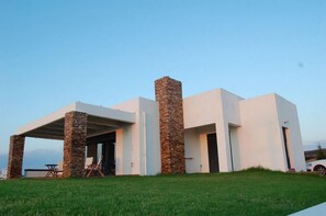 A modern building with a flat roof, stone pillars, and a covered outdoor area with seating. - Cristelia Luxury Sea Front & Pool Villa (Rhodes)