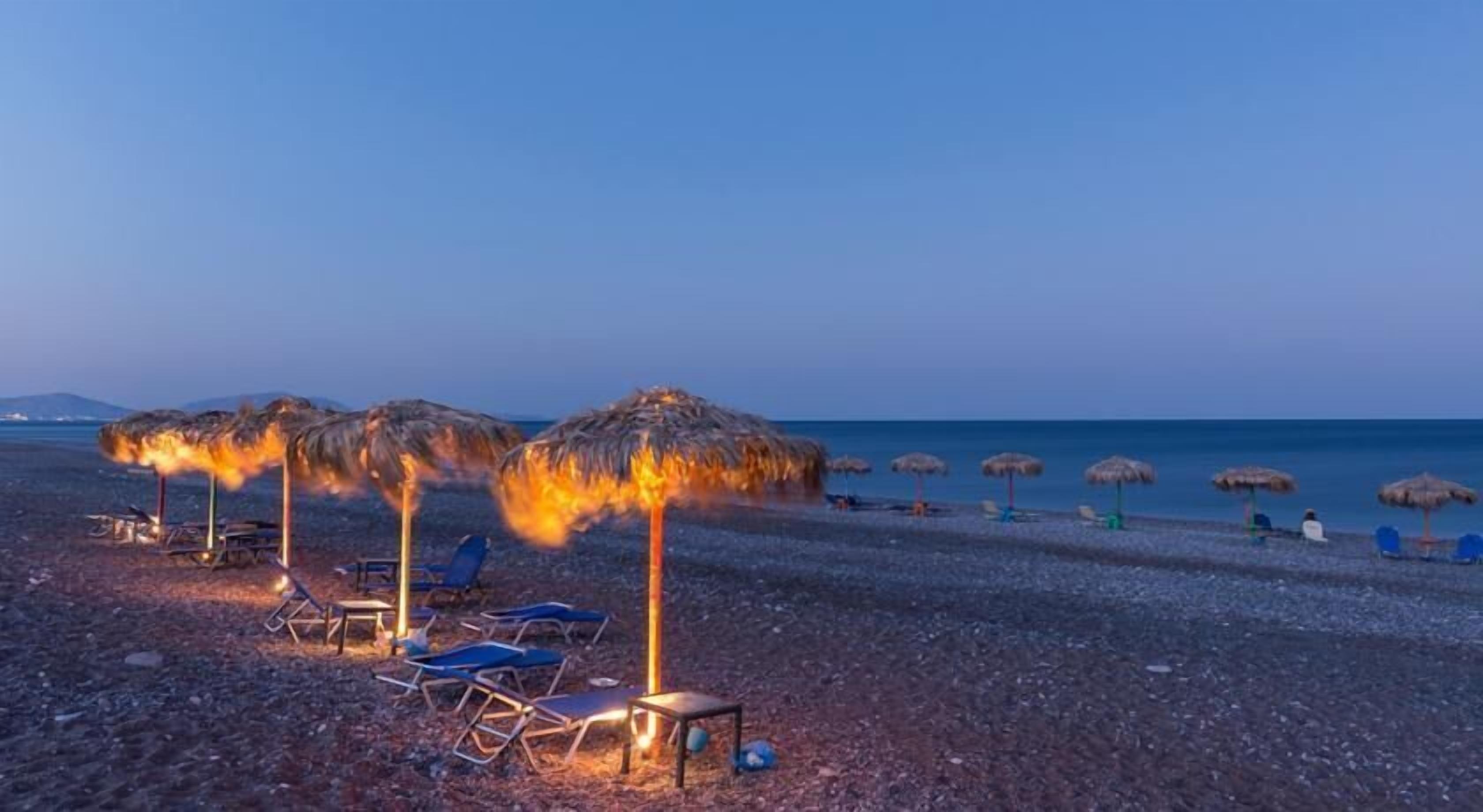 A beach with thatched umbrellas and lounge chairs.