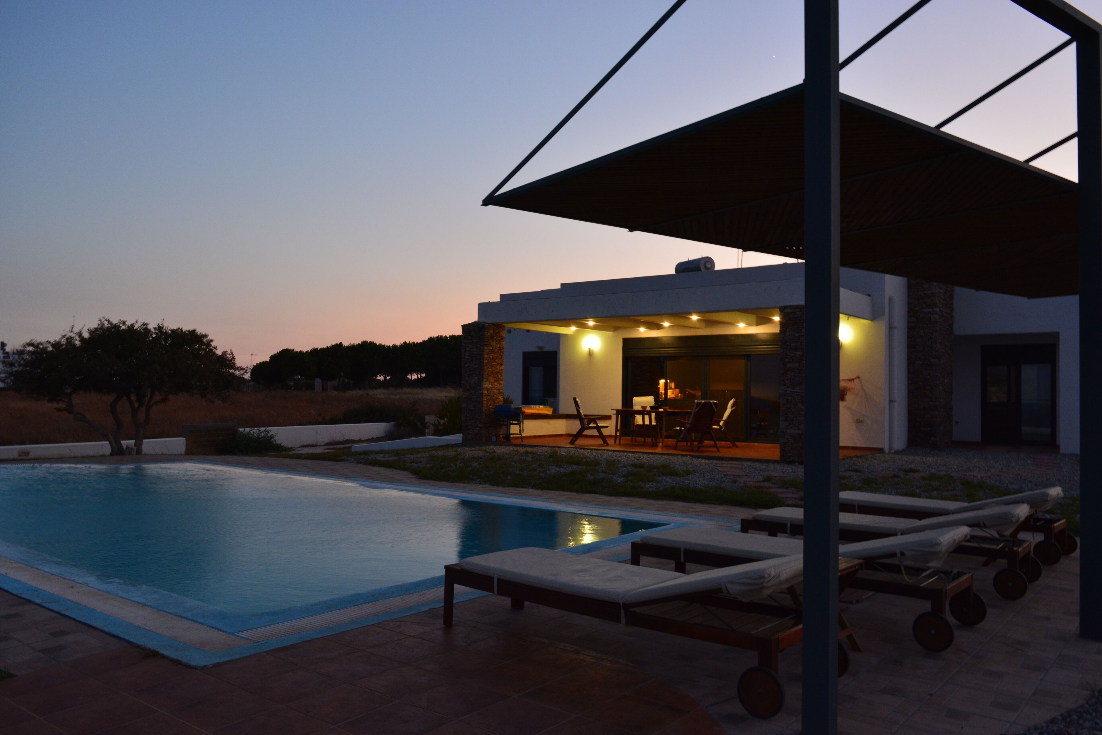 A modern house with a swimming pool, outdoor seating, and a covered patio area.
