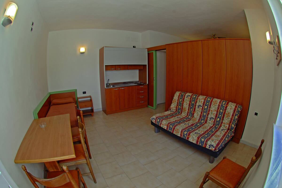 A compact room with a kitchenette, a sofa, a dining table with chairs, and a small cabinet.