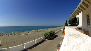 A beach with umbrellas and lounge chairs, a clear sky, and a building with a balcony.