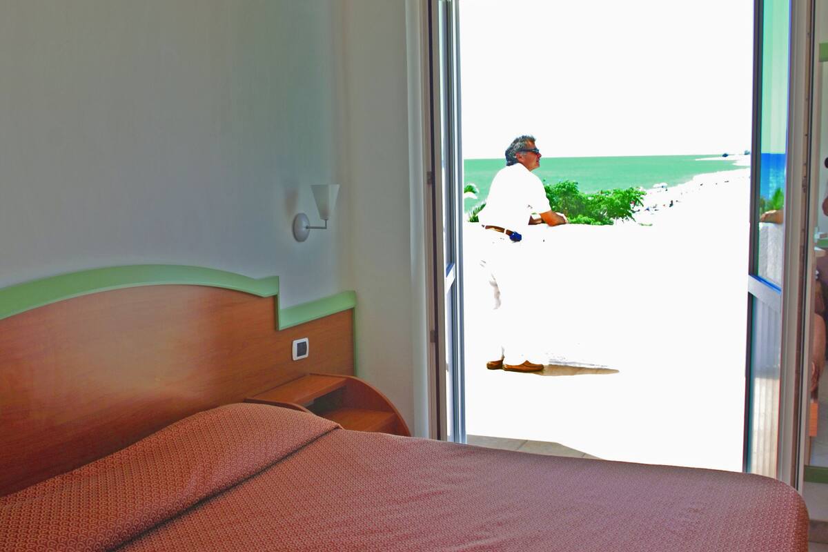 A hotel room with a bed, a view of the beach, and a sliding door.