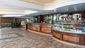 A spacious lobby with a curved reception desk, a coffee machine, and a display case filled with snacks.