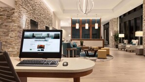 Eine moderne Hotelhalle mit Steinwand, einem runden Tisch mit einem Laptop und einer Sitzecke mit Sofas und Lampen.