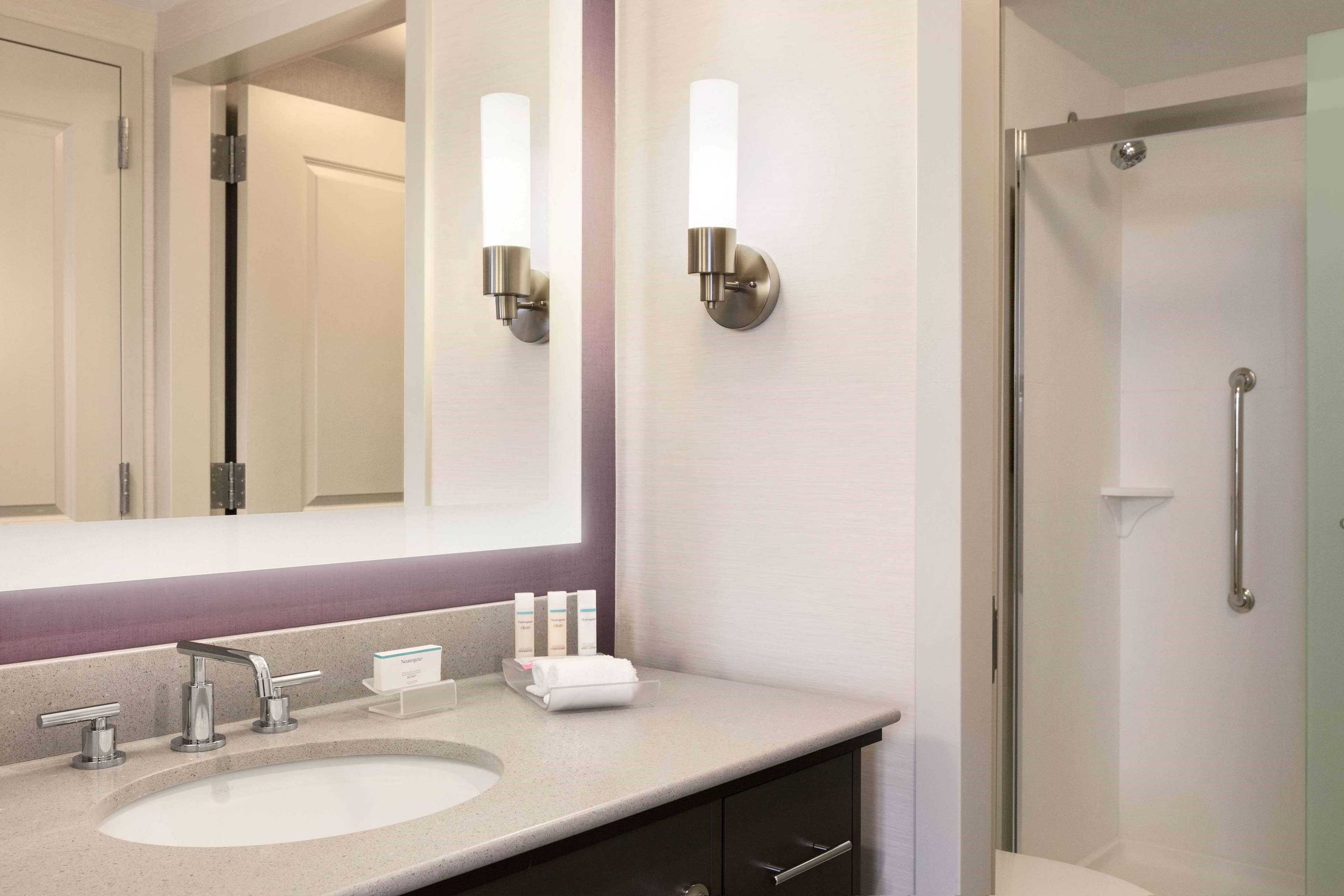 Un baño con un espejo grande, dos luces empotradas, un lavabo con grifo y una zona de ducha.