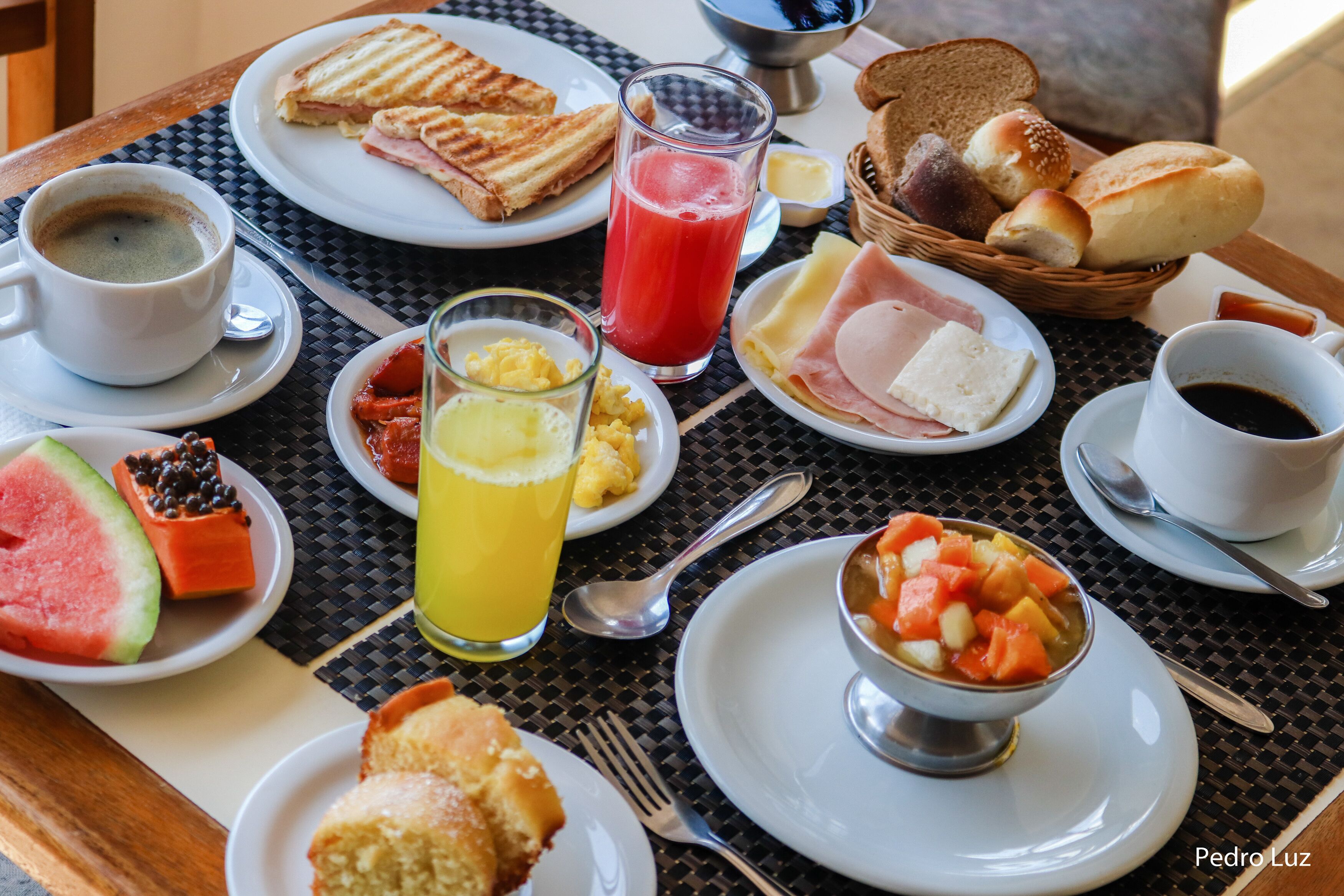 Una mesa de desayuno con diferentes platos, incluyendo tostadas, huevos, jamón y un bol de fruta.