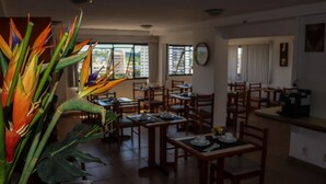 Un comedor con mesas y sillas de madera, un ventanal con vistas, y una planta de hojas coloridas.