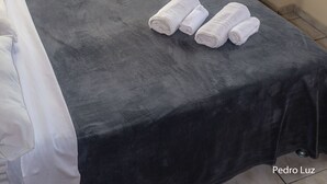 Habitación de hotel con cama, un televisor de pantalla plana montado en la pared, ventana con cortinas y vistas a edificios.