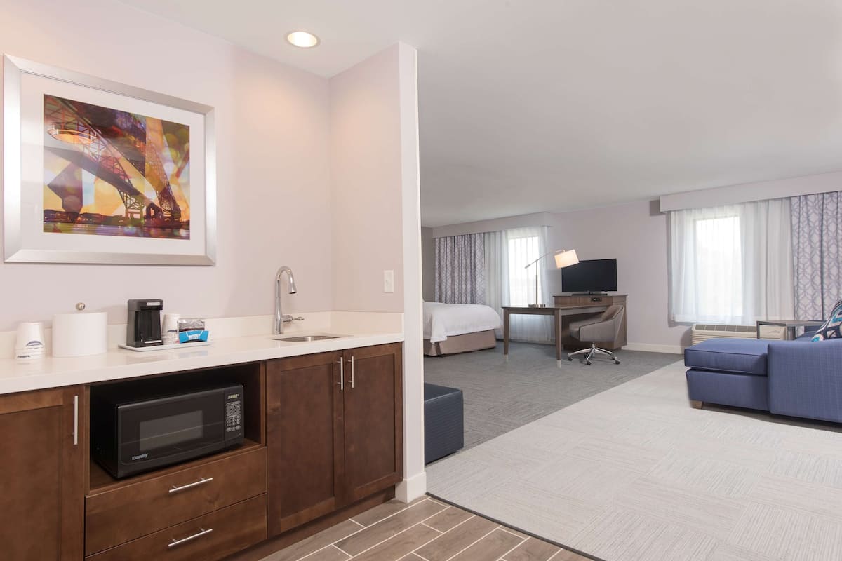 A hotel room with a kitchenette, a bed, a TV, and a sofa.