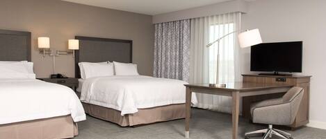 A hotel room with two beds, a desk with a chair, a TV, and a lamp.