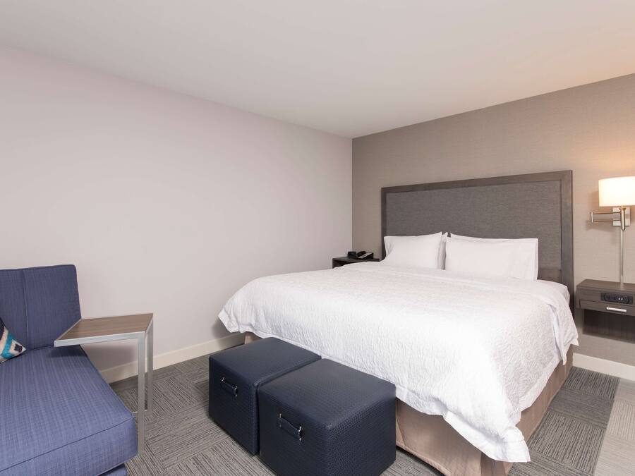 Una habitación de hotel con una cama, una mesita de noche, un sillón, un sofá y dos otomanas.