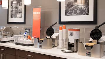 A breakfast bar with waffle makers, coffee machines, and waffle containers.