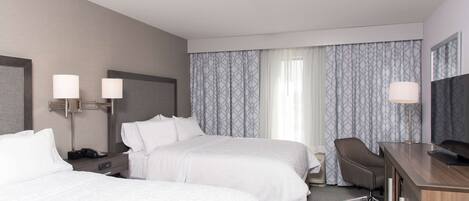 A hotel room with two beds, a desk, a chair, and a television.