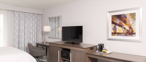 Una habitación de hotel con cama, escritorio con televisor, silla, microondas y cafetera.