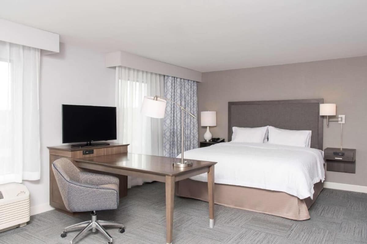 A hotel room with a bed, a desk, a chair, a television, and a nightstand.