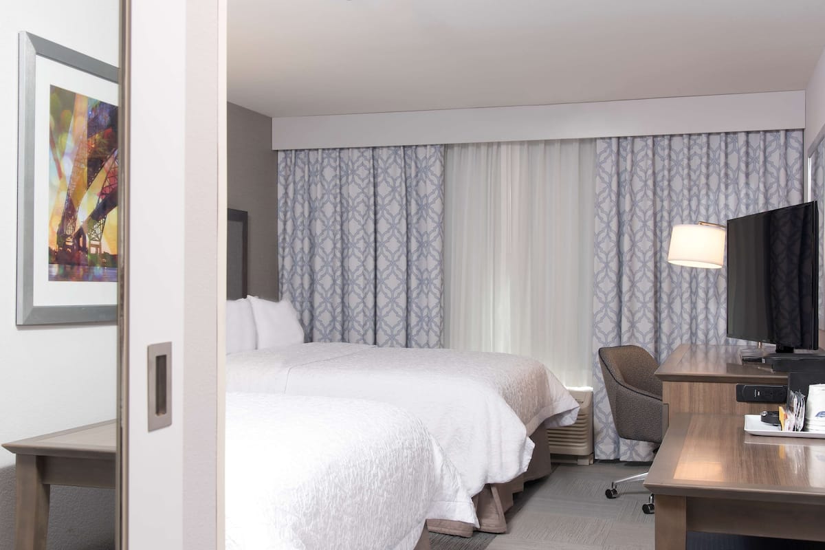 A hotel room with two beds, a desk with a computer, a chair, and a TV.