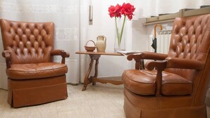 Dos sillones de cuero marrón con una mesa de madera en medio, un florero con flores rojas y un paraguas de madera sobre la mesa.