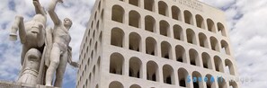 A building with arched windows and a statue of a man with raised arms. - Attico dei Pini (Rome)
