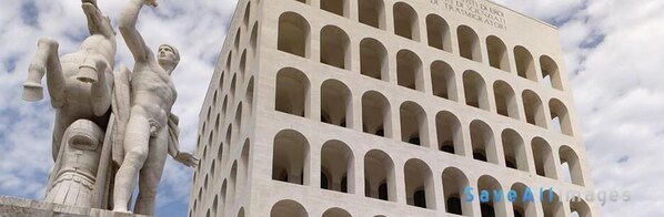 A building with arched windows and a statue of a man with raised arms. - Attico dei Pini (Rome)