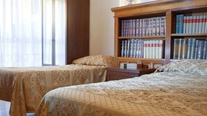 Una habitación con dos camas, una estantería de madera y una ventana con cortinas.