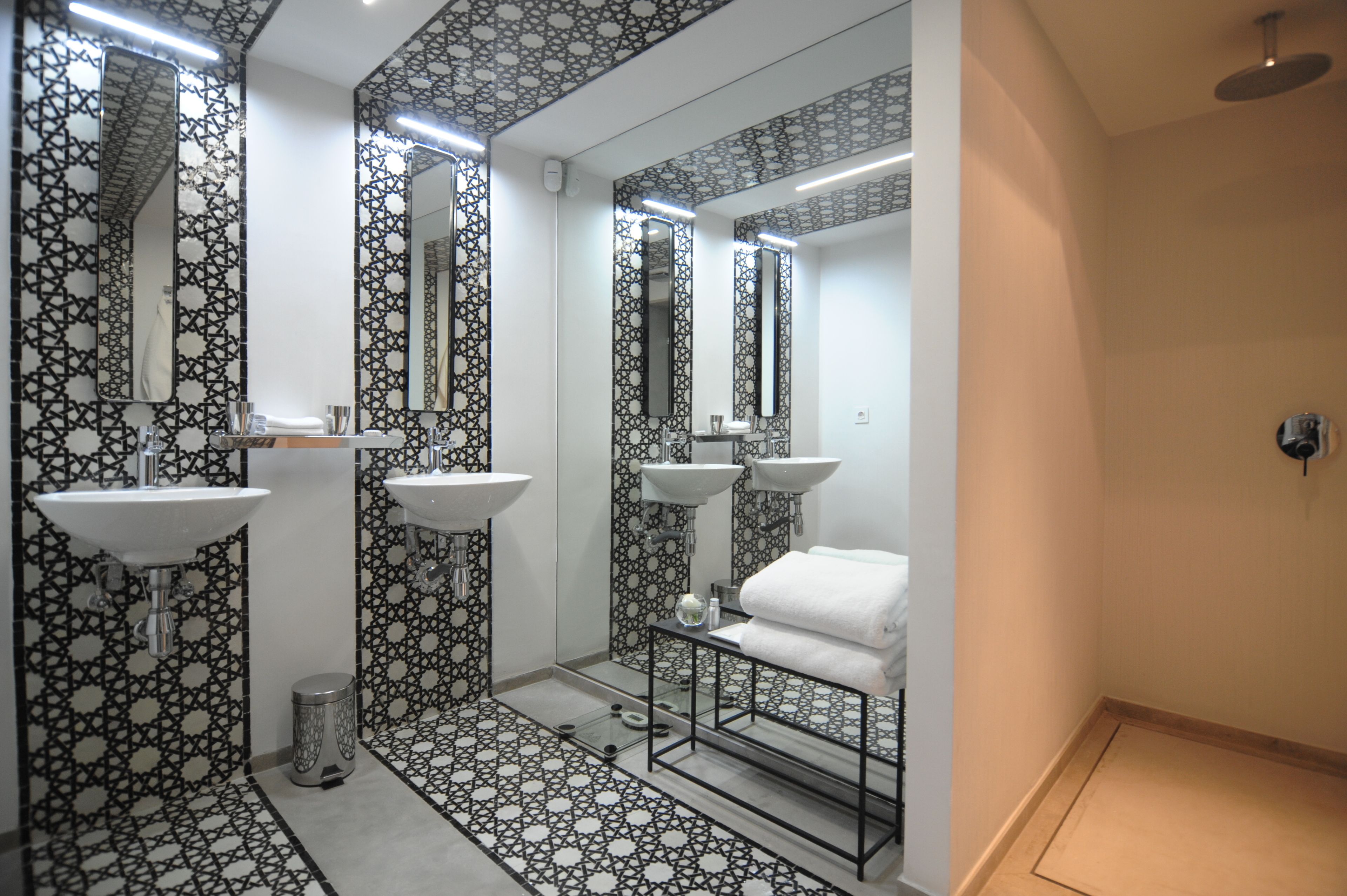 A modern bathroom with three sinks, a glass shower enclosure, and patterned tile flooring.
