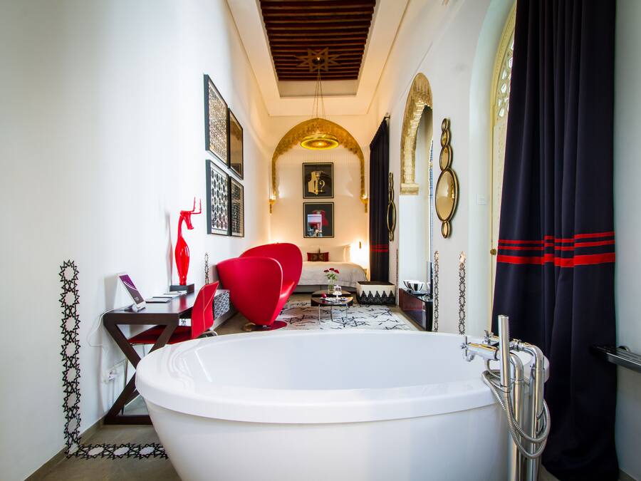 Une salle de bain moderne avec une grande baignoire, une chaise rouge et un lit avec une tête de lit blanche.