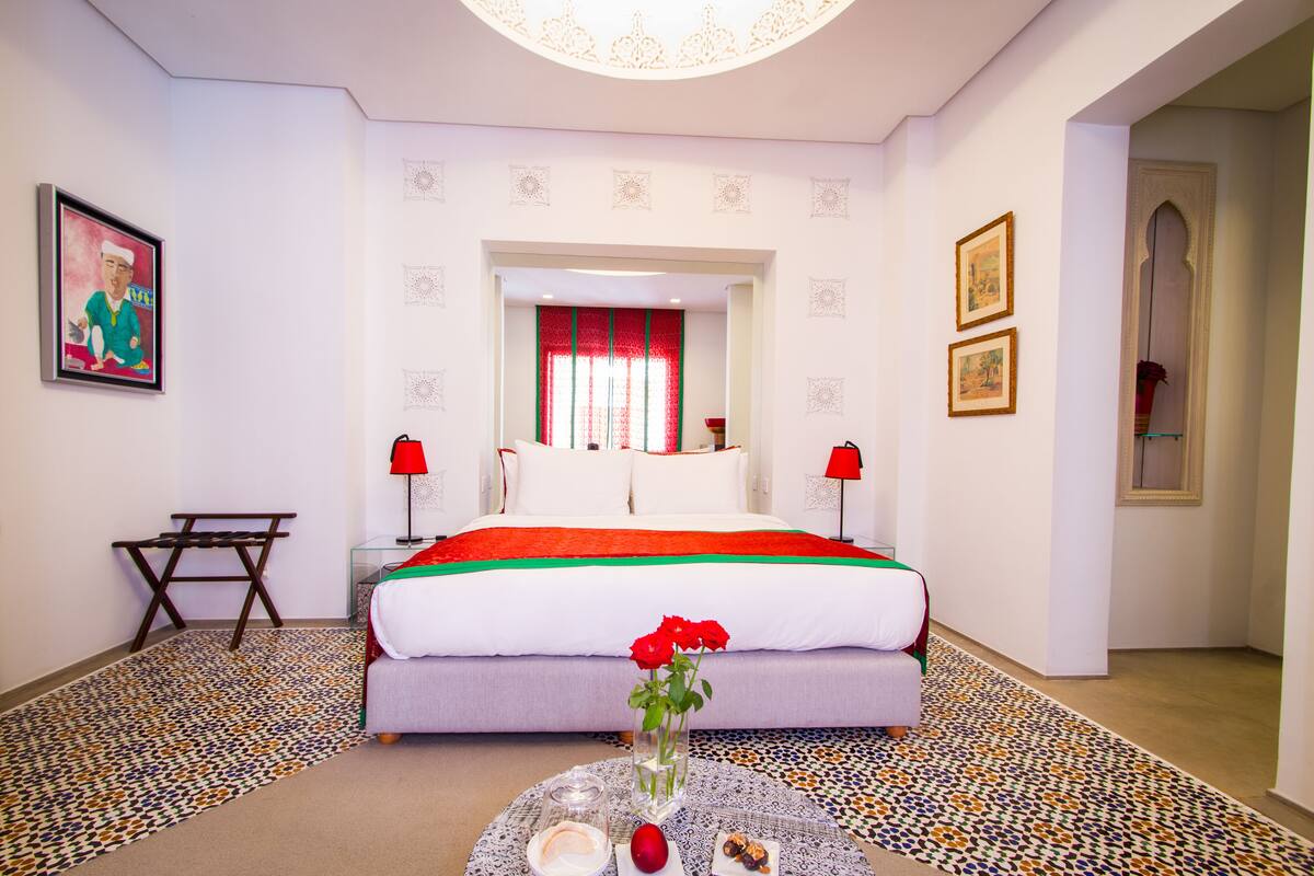 A hotel room with a bed, a small table with a vase of flowers, and a patterned rug.