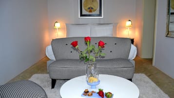 Una sala de estar con un sofá a cuadros, una mesa de centro redonda con aperitivos y un jarrón de flores, y dos lámparas de pared.
