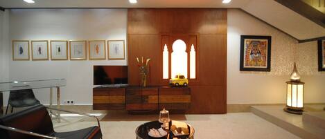 A modern living room with a glass table, a sofa, a decorative cabinet, and a television.