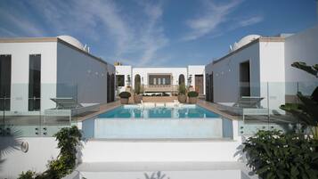 Uma área de piscina moderna com céu claro, cercada por paredes brancas e plantas em vasos.
