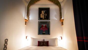 A hotel room with a bed, two framed artworks, a decorative arch, and a curtain.