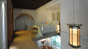 Un intérieur moderne avec un pont de verre reliant deux niveaux, une lanterne suspendue et une vue sur une chambre à coucher avec un lit et une fenêtre.