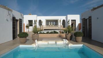 A pool area with a clear blue pool, white walls, and potted plants.
