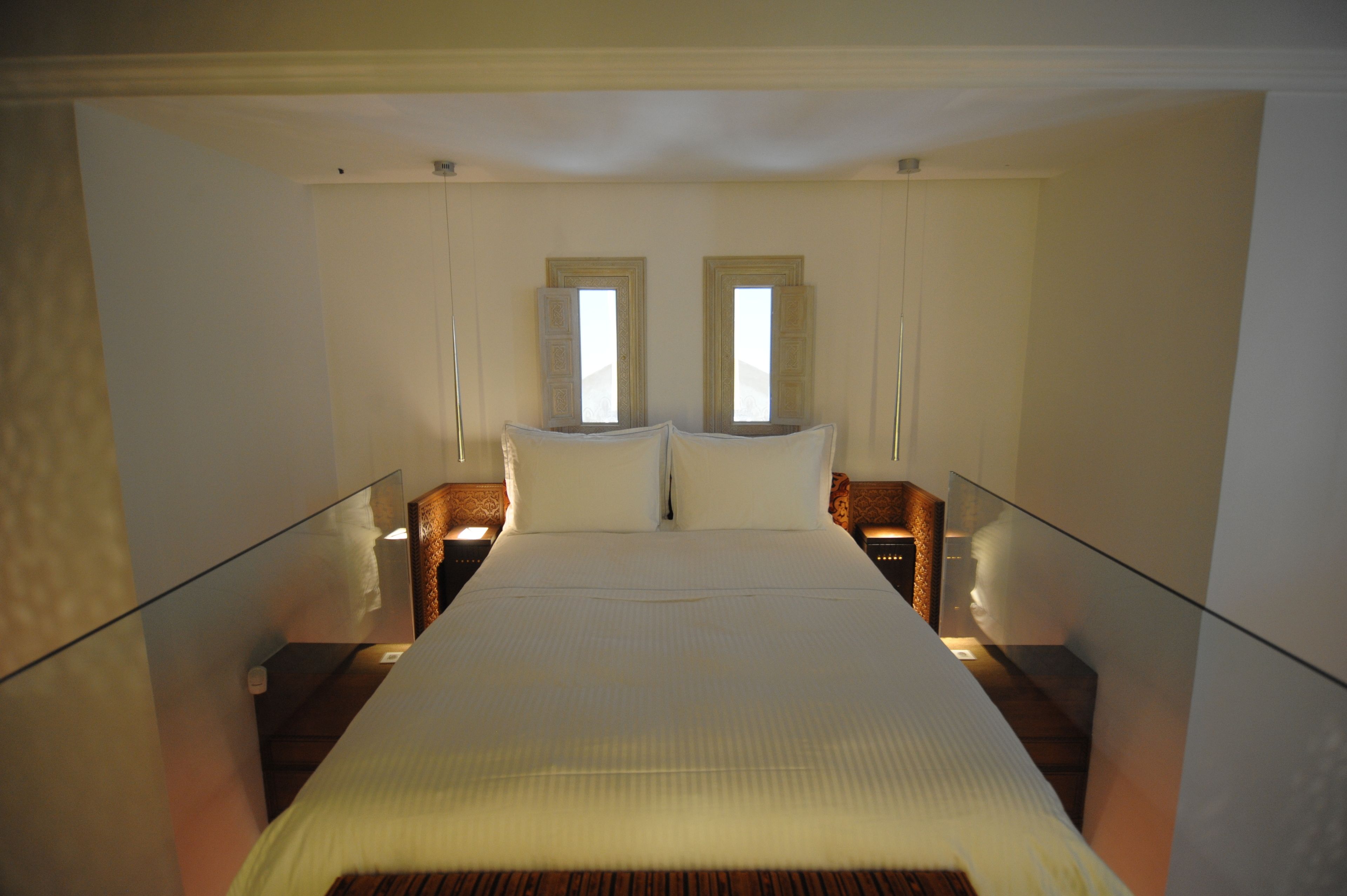 A hotel room with a large bed, two bedside tables, and two windows.