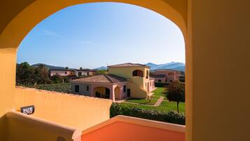 A view through an archway of a residential area with houses, a well-maintained lawn, and distant mountains.