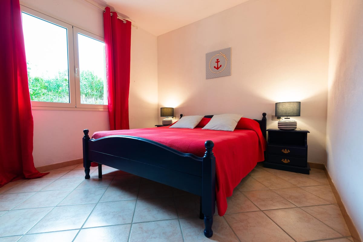 A bedroom with a bed, two bedside tables, a window with curtains, and a wall decoration.