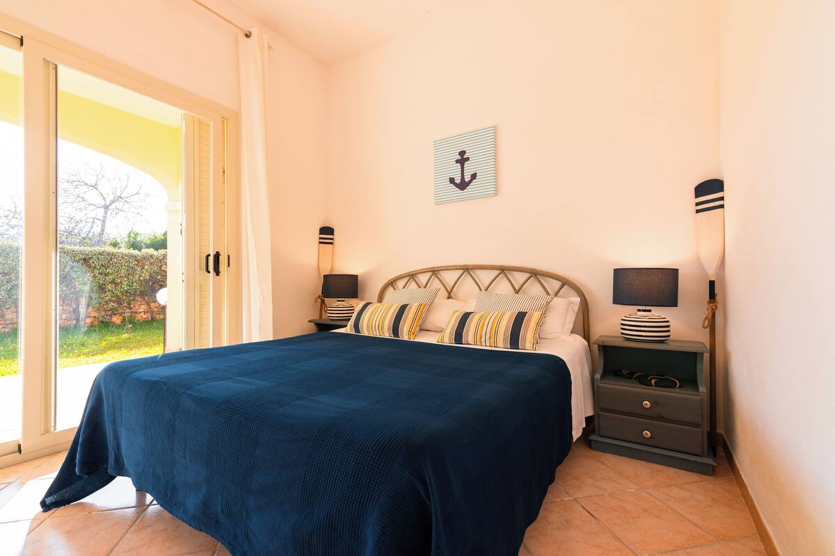 A bedroom with a bed, nightstands, and a view of the outdoors.