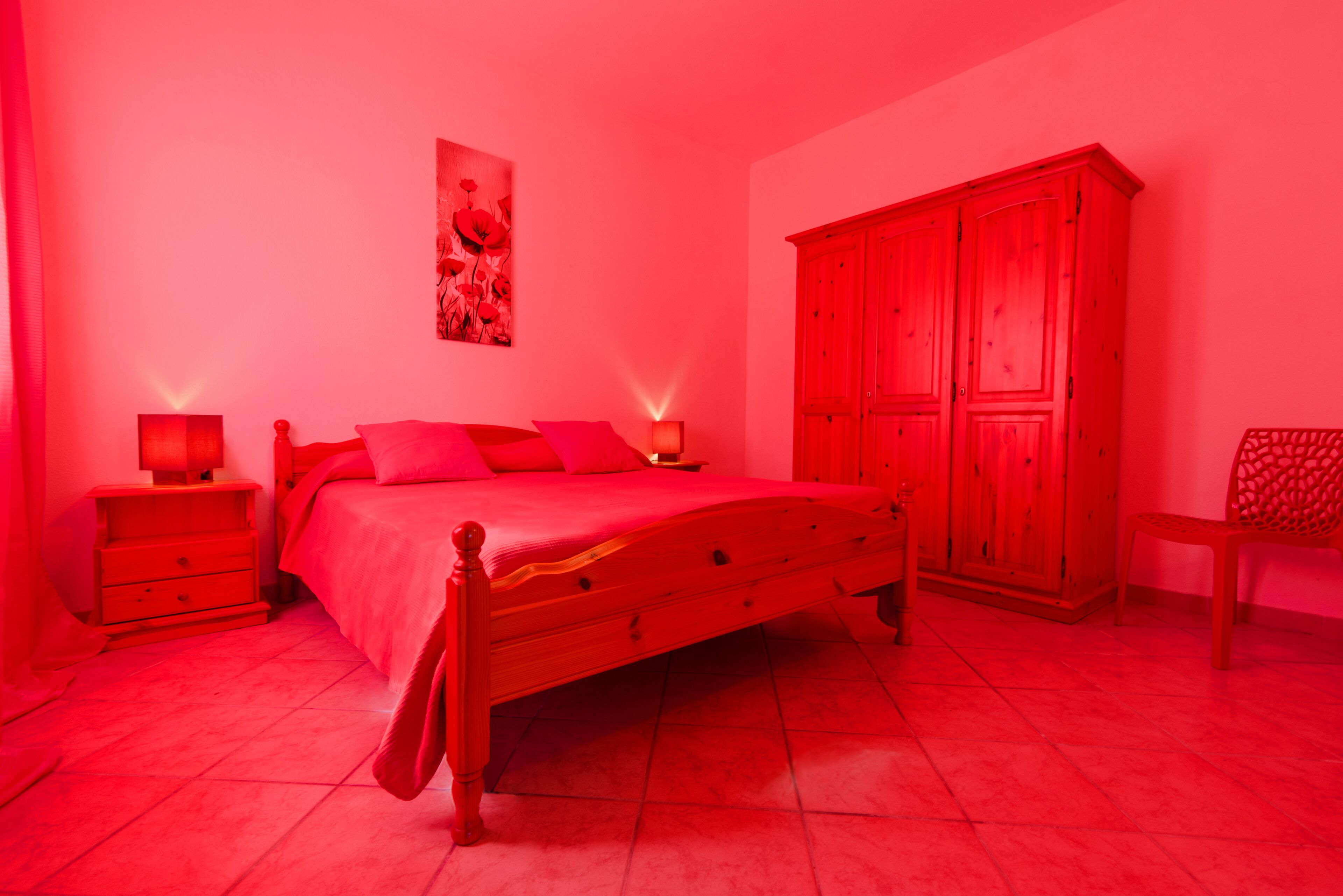 Ein Schlafzimmer mit einem hölzernen Bett, zwei Nachttischen mit Lampen, einem Kleiderschrank und einem Sessel.