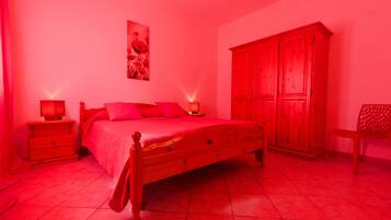 Ein Schlafzimmer mit einem hölzernen Bett, zwei Nachttischen mit Lampen, einem Kleiderschrank und einem Sessel.