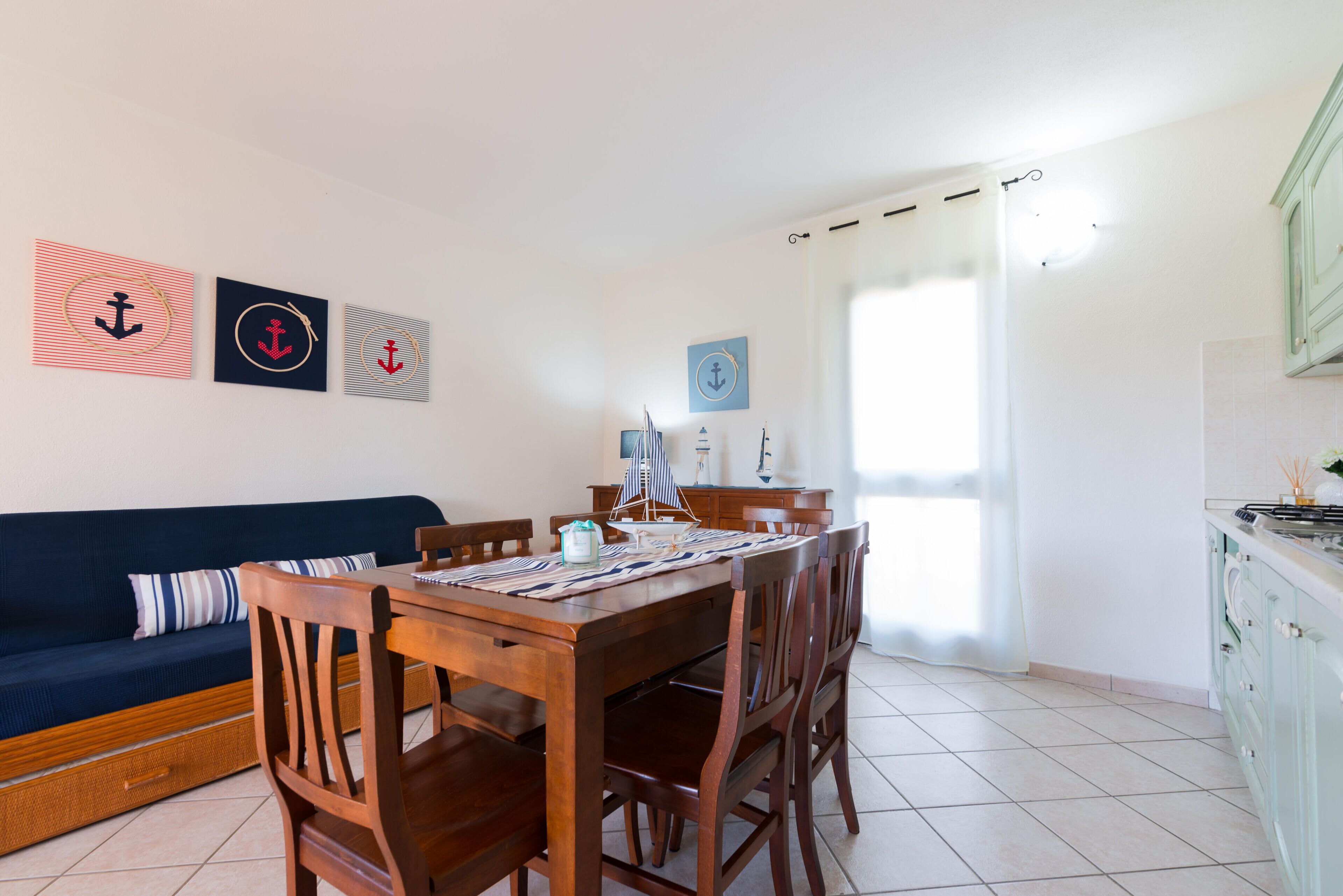 Uma sala de jantar com uma mesa e cadeiras de madeira, um sofá azul e arte nas paredes com tema náutico.
