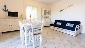 Una habitación con una mesa de comedor, sillas, un televisor, un armario, un sofá y una pared decorada con una pala y un ancla.
