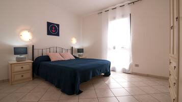 Ein Schlafzimmer mit Bett, Nachttischen, einer Wandleuchte und einem Fenster mit Vorhängen.