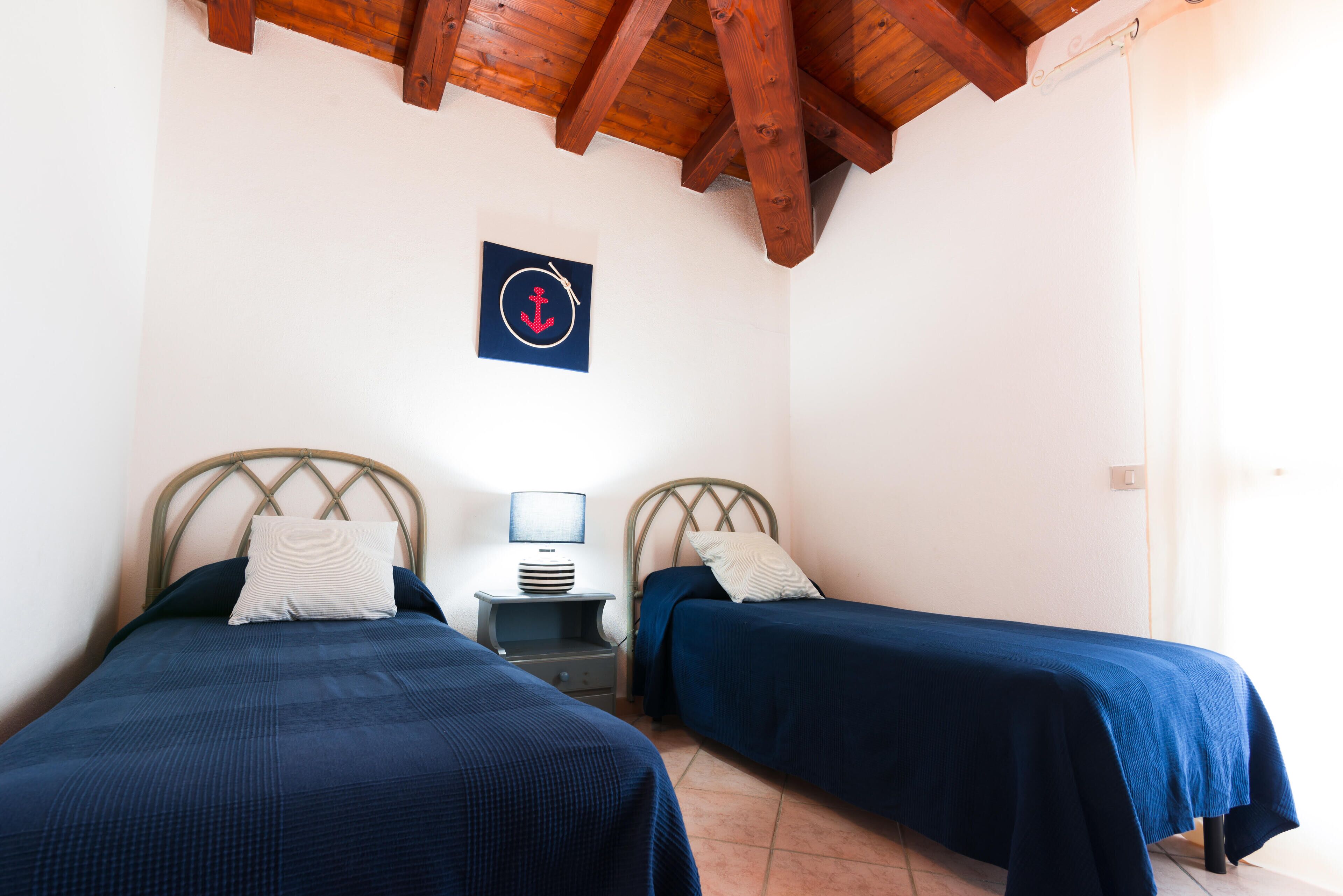 A room with two beds, a nightstand, a lamp, and a wall-mounted anchor decoration.