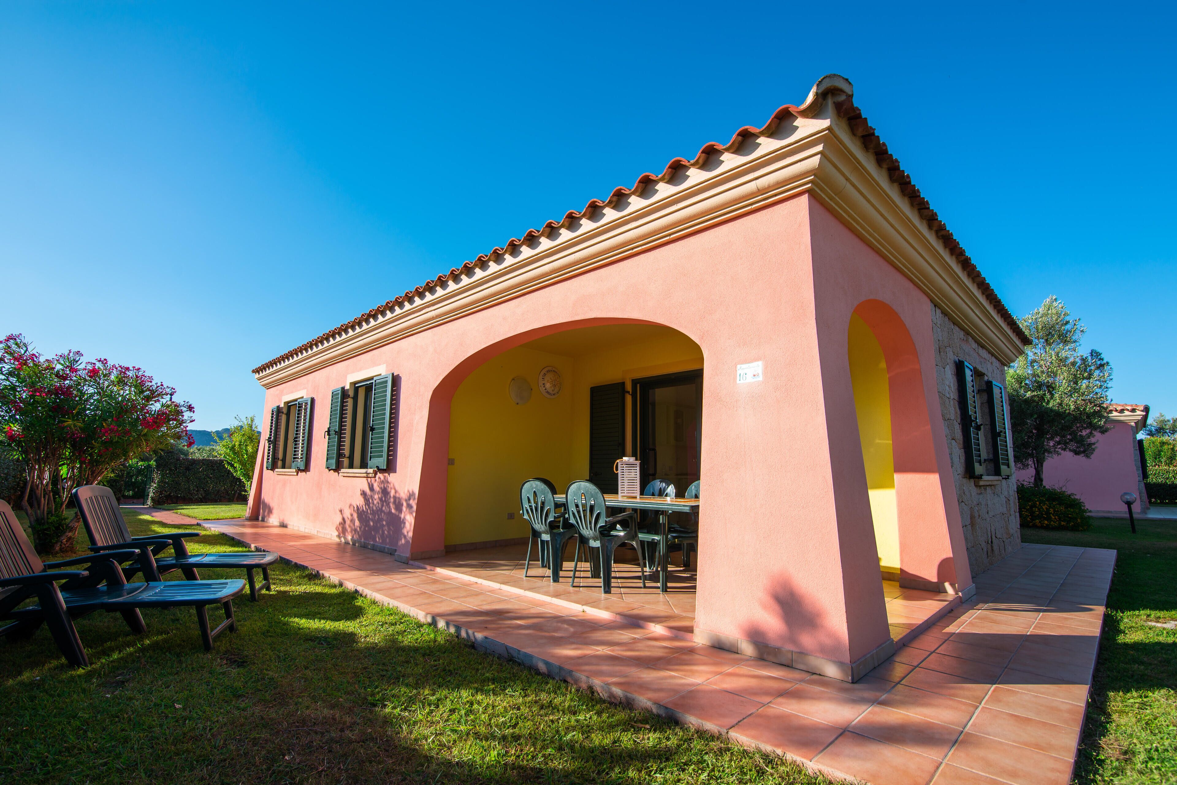 Une villa rose dotée d’un patio carrelé, d’un espace salon extérieur et surplombant un ciel d’un bleu limpide.